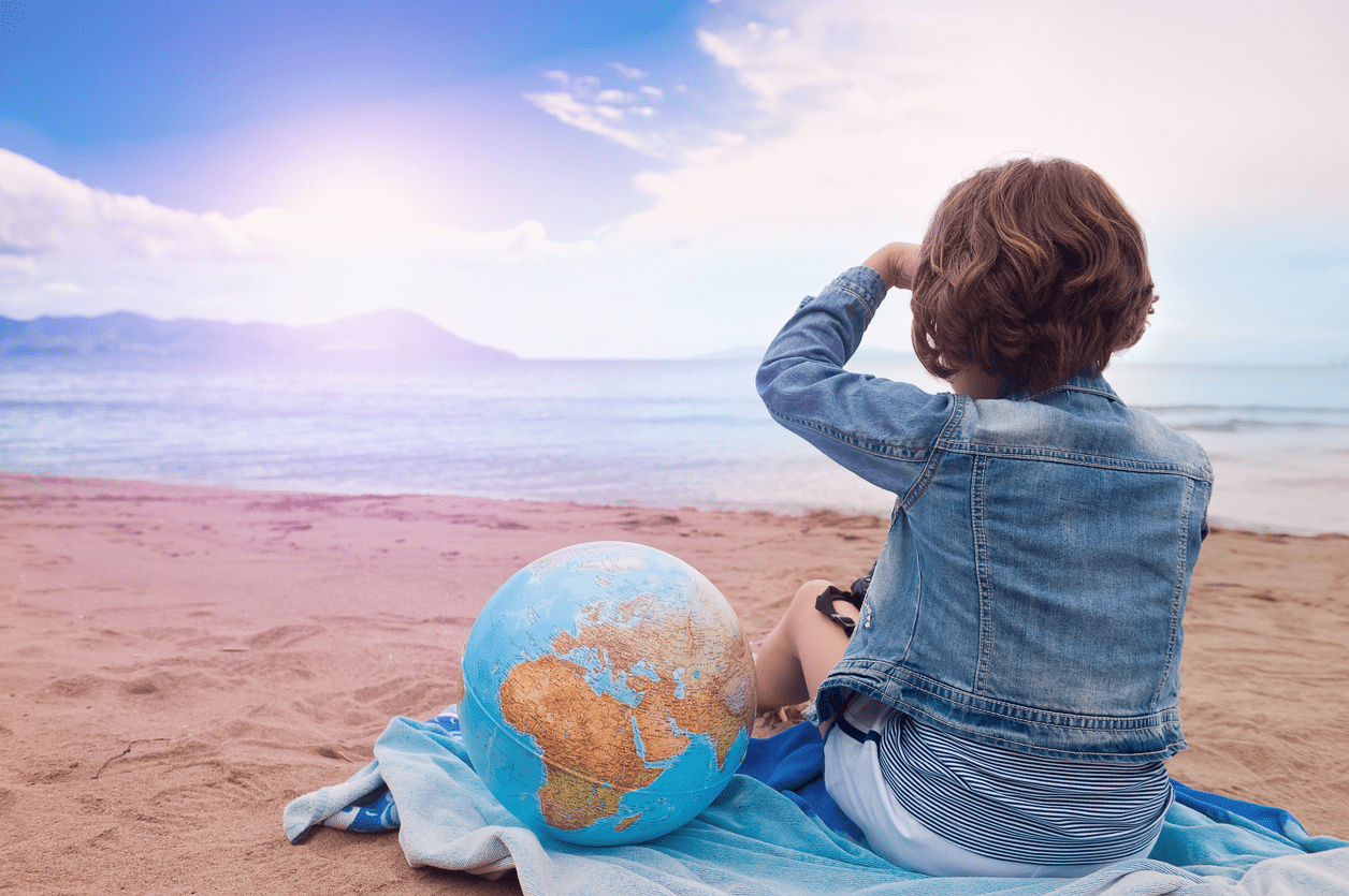 A child sitting on the beach with a globe