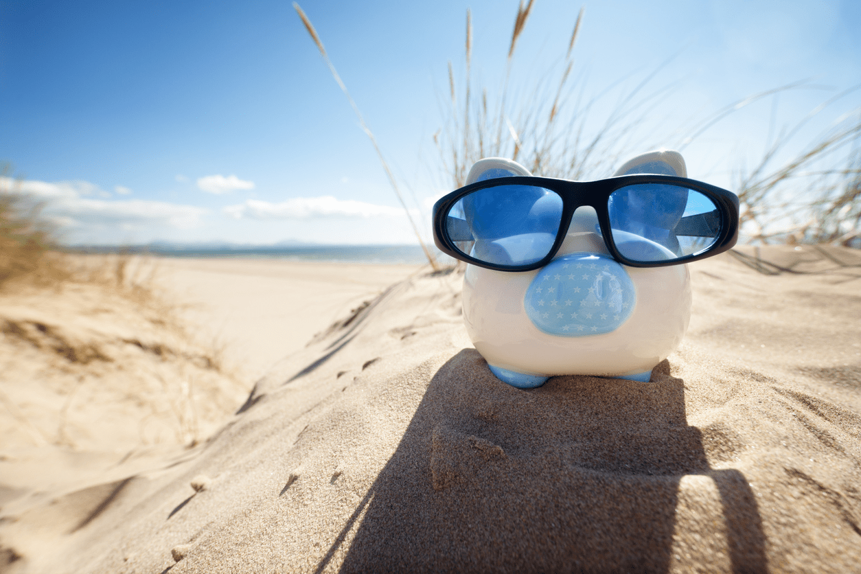 A piggy bank with sunglasses on top of the beach.